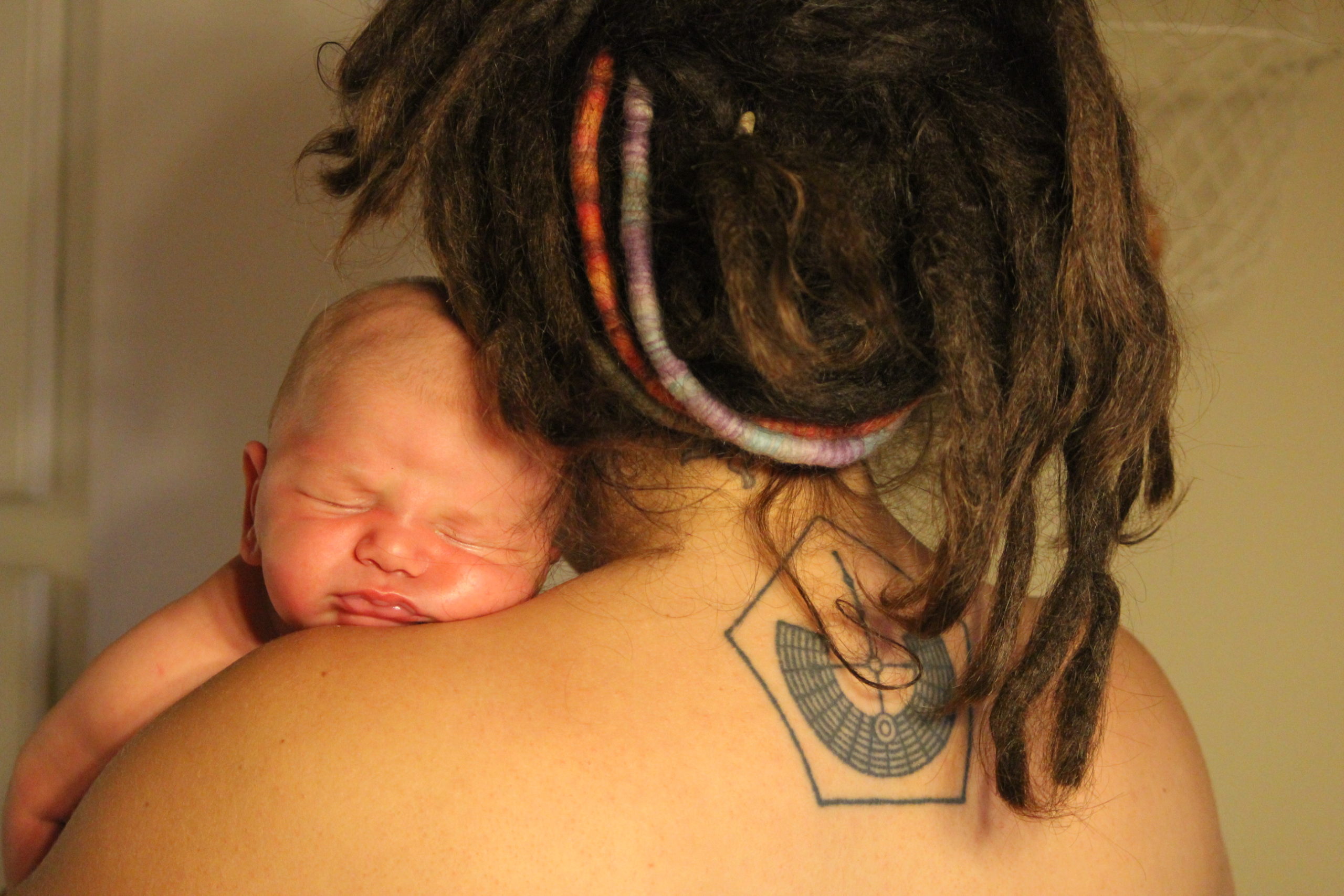 Woman with dreadlocks and Burning Man tattoo holds a newborn baby